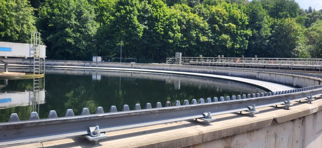 Rundes Nachklärbecken einer Kläranlage mit ruhiger Wasseroberfläche und umlaufender Räumvorrichtung zur Abwasserbehandlung.