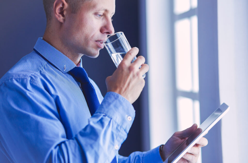 Geschäftsmann trinkt ein Glas Wasser und überwacht auf seinem Tablett die Temperaturen an den Wasserentnahmestellen.