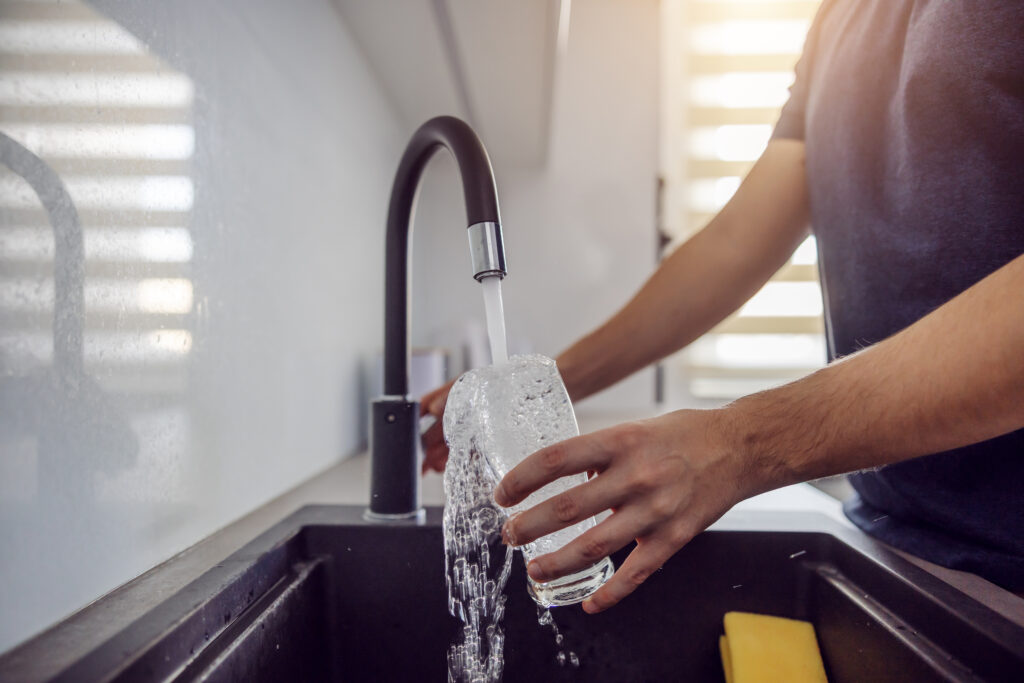 Ein Mann füllt ein Glas Wasser am Wasserhahn.