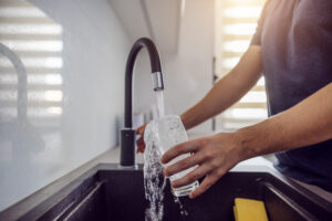 Ein Mann füllt ein Glas Wasser am Wasserhahn.